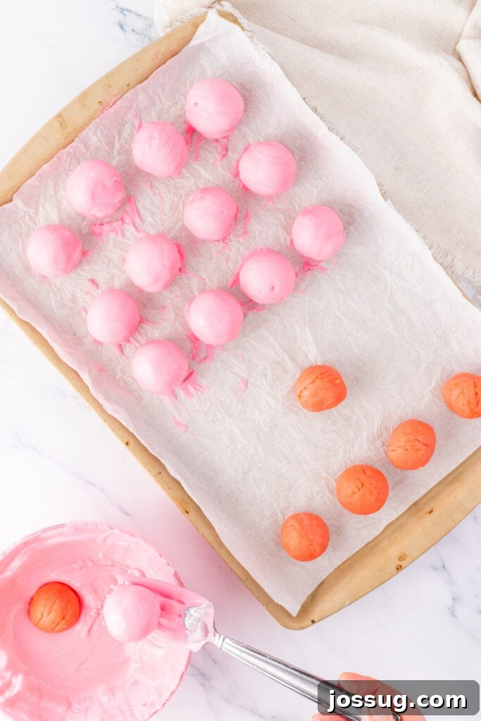 Pink truffle balls arranged on parchment paper with some freshly dipped in pink coating and others waiting to be coated.