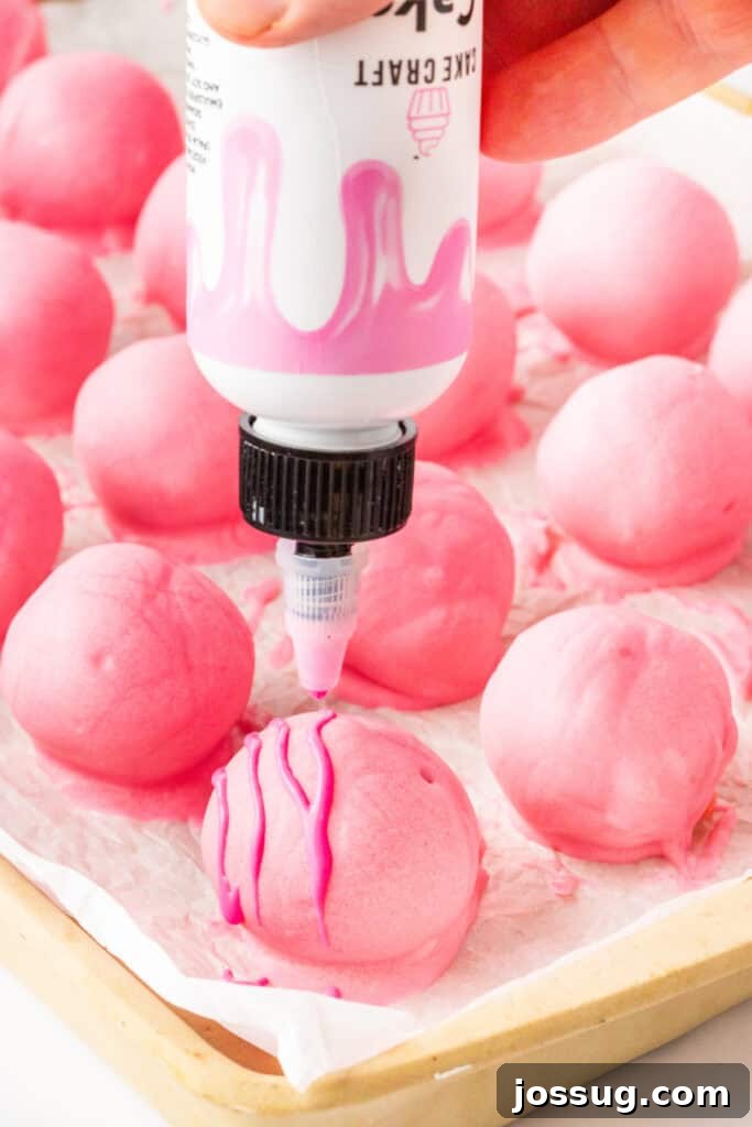 Pink Valentine truffles being drizzled with pink candy coating while resting on parchment paper.