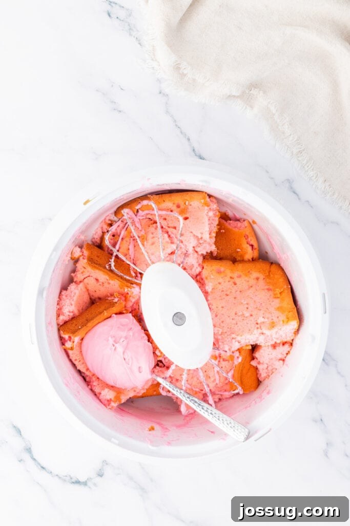Bowl of pink cake pieces and frosting being mixed together with a spoon to create truffle filling.