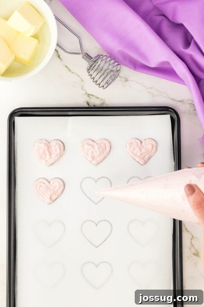 Piping heart-shaped macaron batter onto parchment paper using a heart template.