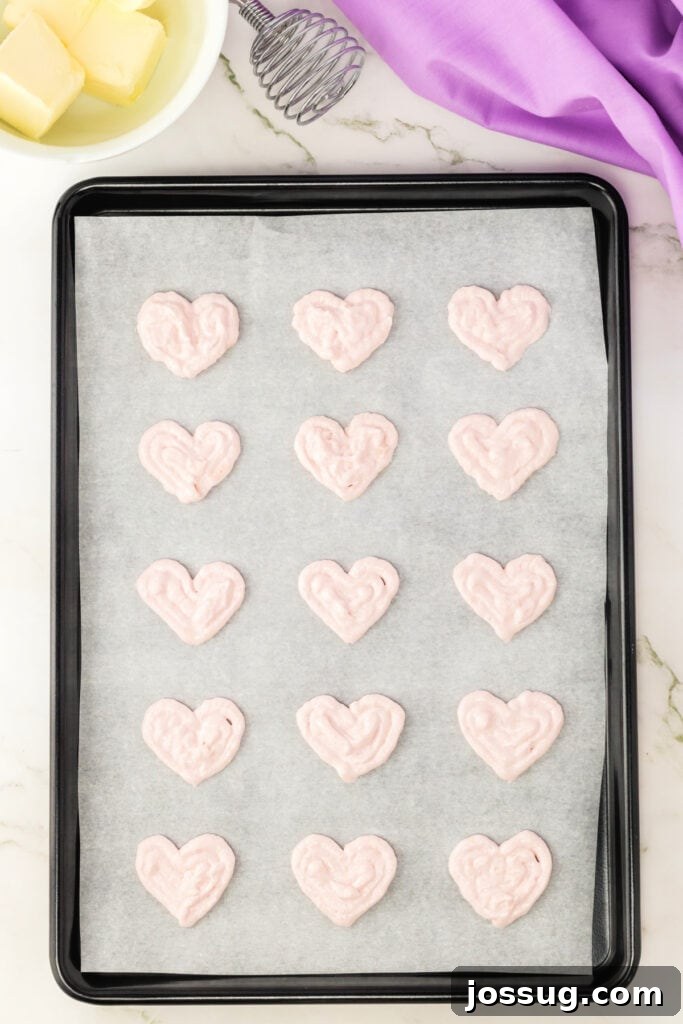 Heart-shaped macaron shells resting on parchment paper before baking.