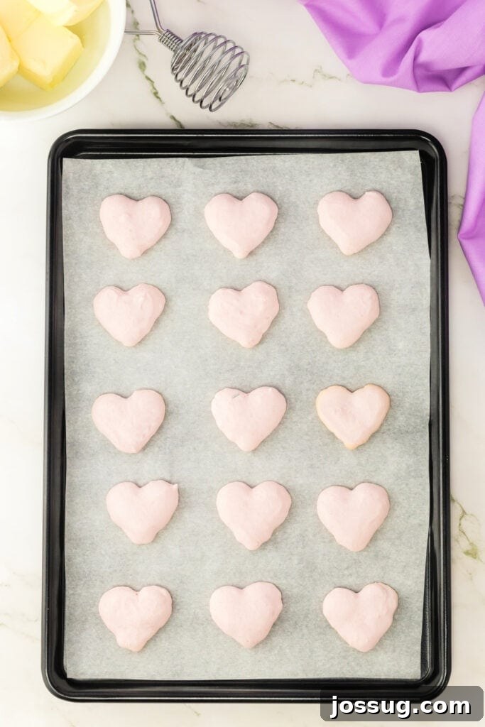 Heart-shaped pink macaron shells resting on parchment paper on a baking sheet after baking.