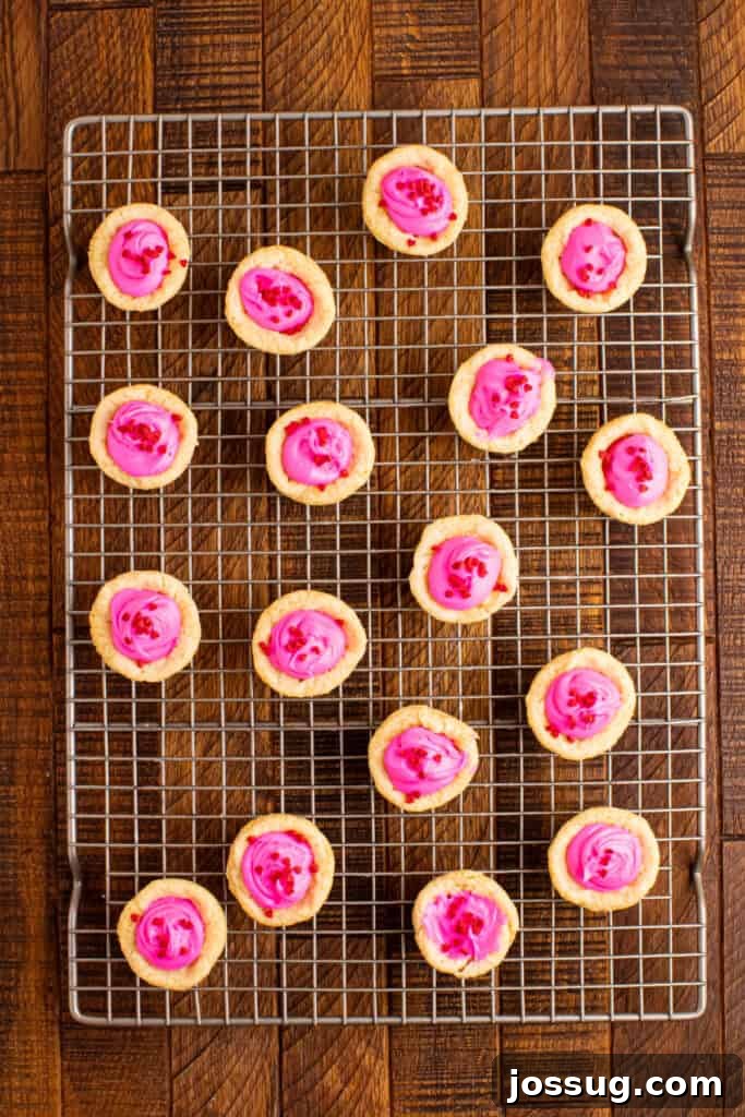 Valentine's Day Sugar Cookie Cups 5 Valentine sugar cookie cups cooling on a wire rack with pink frosting and red heart sprinkles