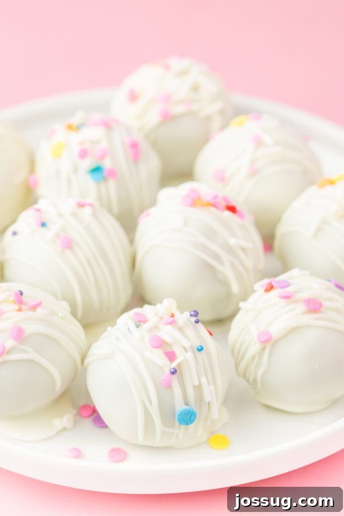 Birthday Cake Bites 2 White chocolate coated birthday cake truffles decorated with pastel sprinkles on a white plate against a pink background