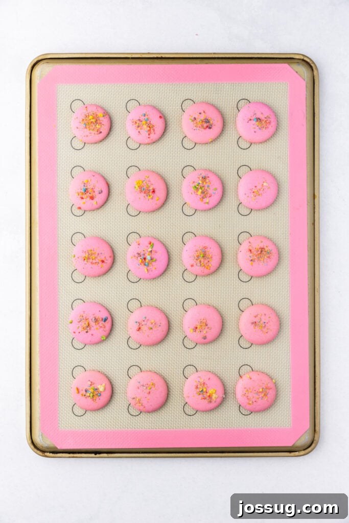 Pink macaron shells baked and set on a silicone mat with cereal topping visible