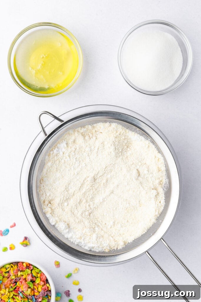 Overhead view of sifted almond flour and powdered sugar in a mesh sieve, with egg whites and granulated sugar measured in small bowls