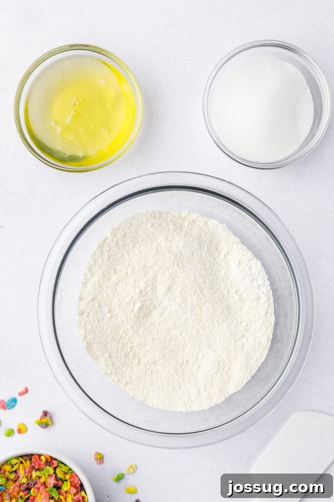 Almond flour and powdered sugar sifted into a clear mixing bowl, with egg whites and sugar measured above