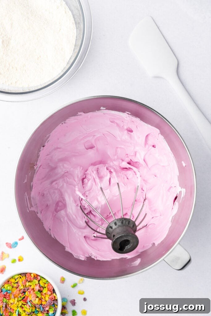 Pink colored meringue in a stand mixer bowl after adding gel food coloring