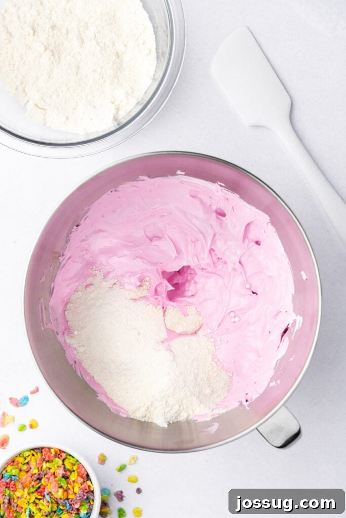 Almond flour and powdered sugar added to pink meringue in a stand mixer bowl