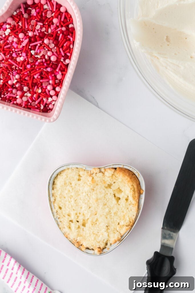 Valentine's Day Mini Treat Cake 15 Heart shaped vanilla cake with the top leveled, sitting on a white cutting board next to a spatula