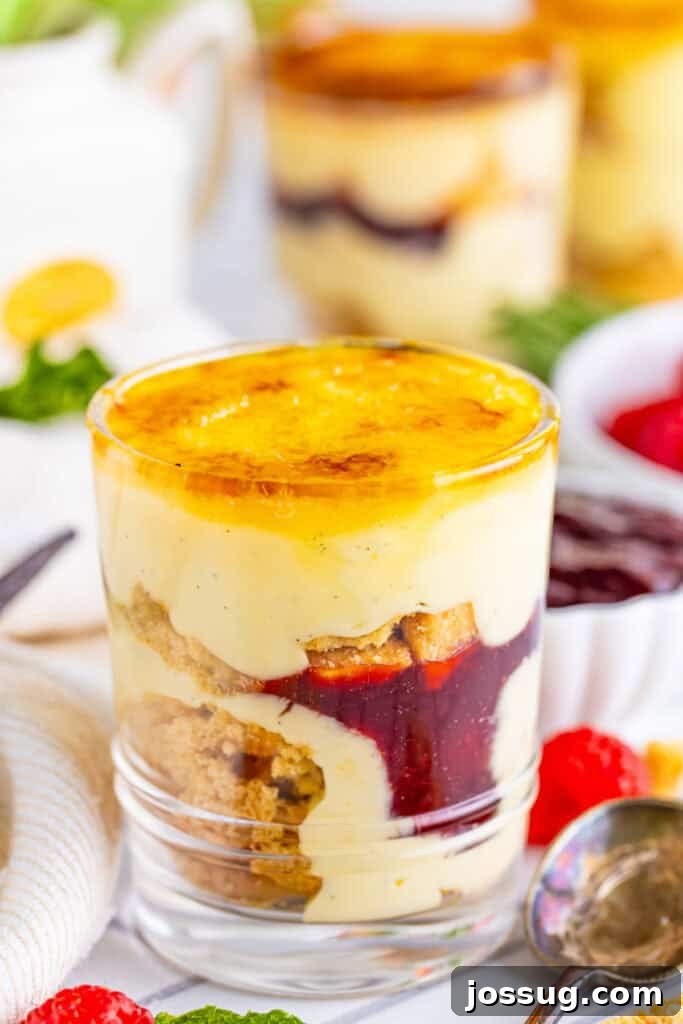 Creme Brulee Dream Trifle 2 Creme brulee trifle in a clear glass, showcasing layers of vanilla custard, shortbread cookies, raspberry jam, and a perfectly caramelized sugar top.