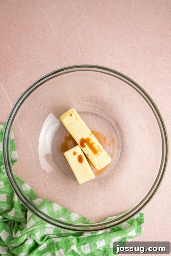 Buttercream Bliss Bites 3 Sticks of butter and vanilla extract in a glass mixing bowl on a pink background