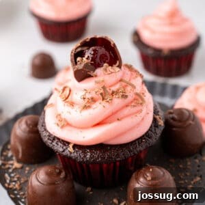 Close up view of a chocolate cupcake with pink frosting and a halved cherry cordial candy on top