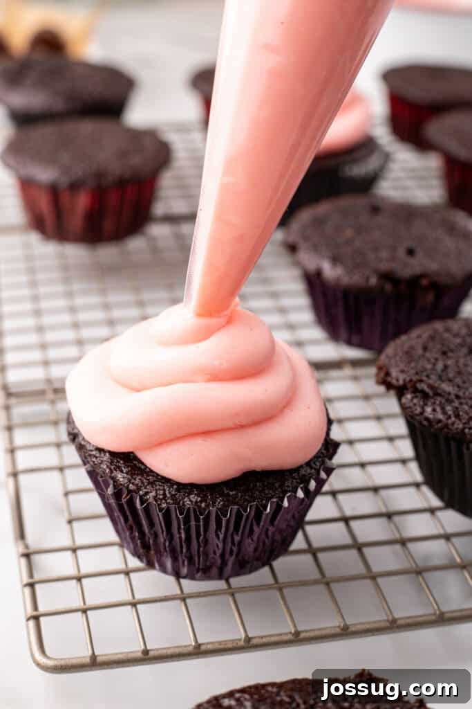 Close up view of pink frosting being piped onto a chocolate cupcake