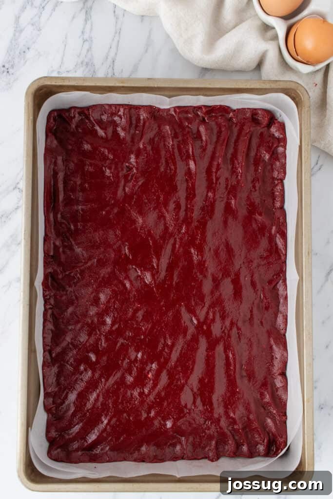 Red velvet brownie batter in a parchment-lined baking pan