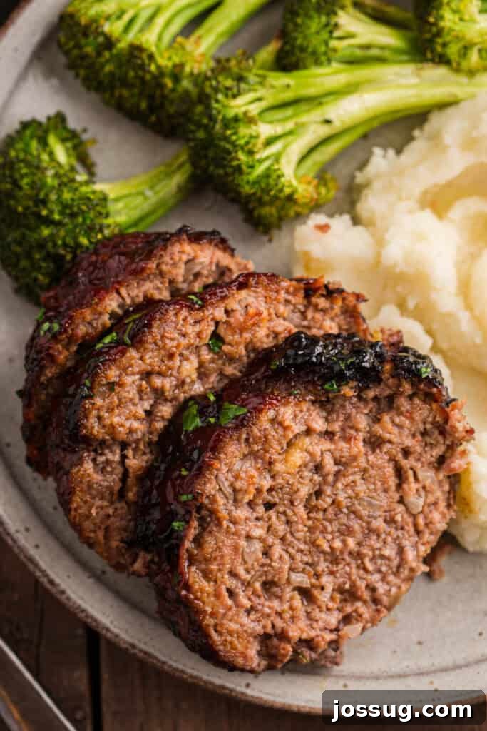 Close up of sliced meatloaf with mashed potatoes and broccoli on a plate.