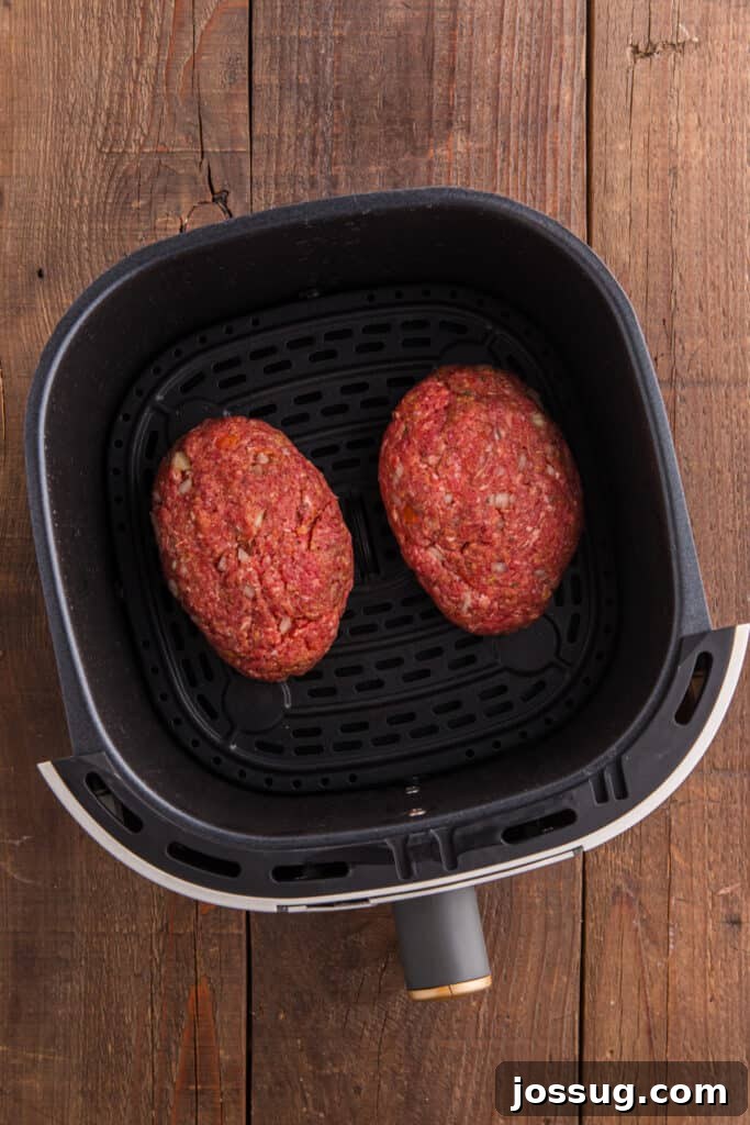 Two shaped raw meatloaves placed inside an air fryer basket.