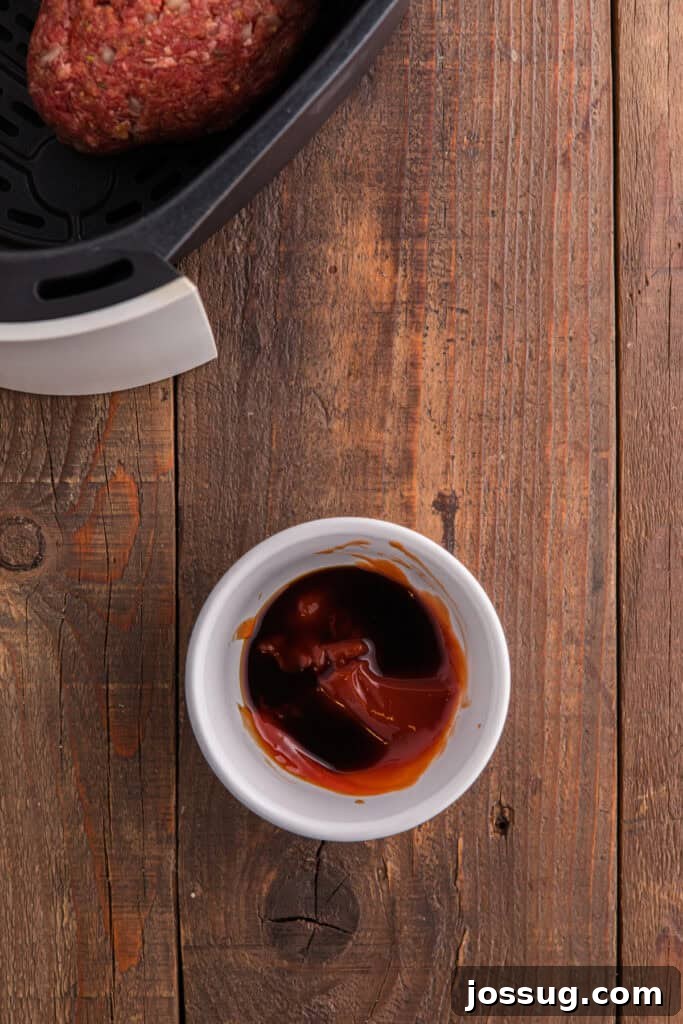 Small white bowl with ketchup and Worcestershire sauce mixture on a wooden surface next to an air fryer basket.