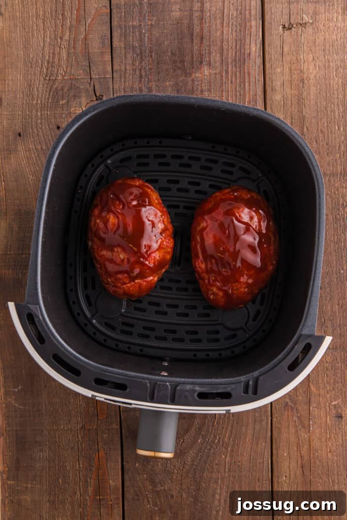 Two raw meatloaves in an air fryer basket topped with ketchup glaze.