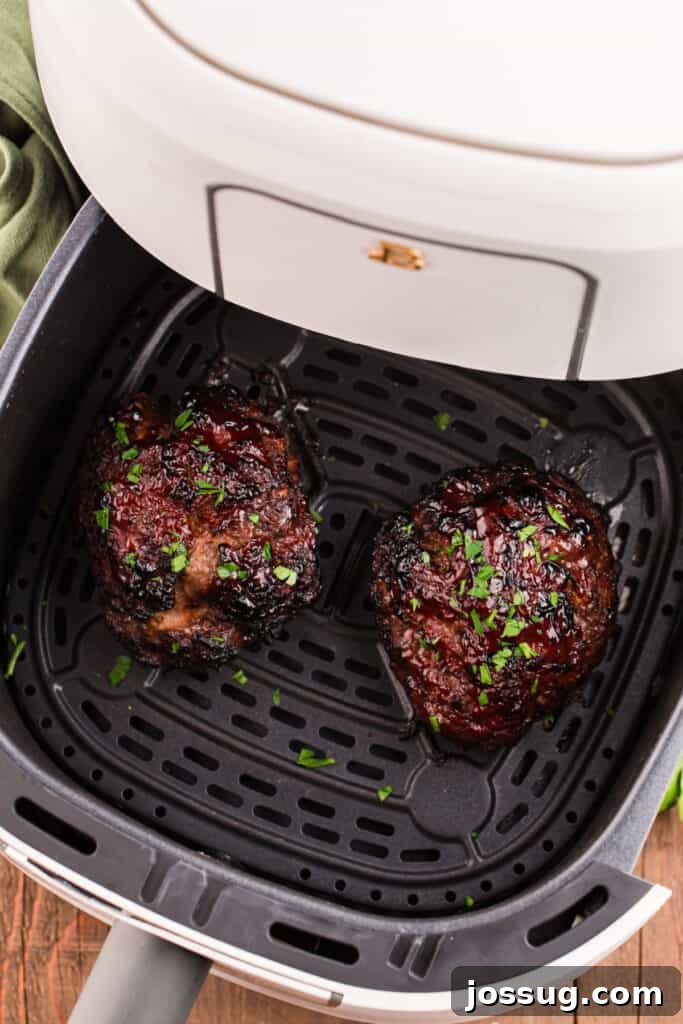 Two cooked glazed meatloaves inside an air fryer basket sprinkled with chopped parsley.