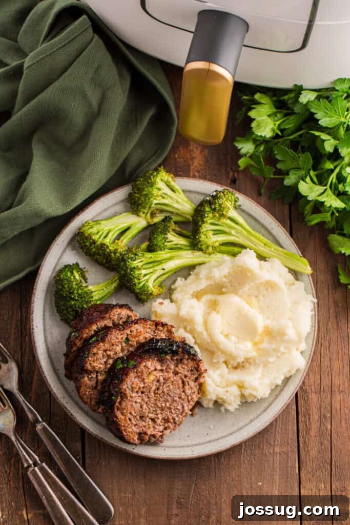 Plate with sliced meatloaf, mashed potatoes, and broccoli next to an air fryer on a wooden table.
