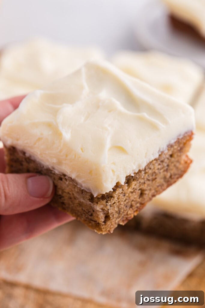 Banana Bread Brownies 16 Hand holding a square of banana brownie topped with cream cheese frosting