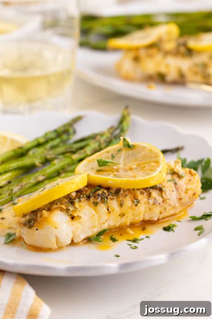 Lemon Garlic Baked Cod on a white plate with asparagus and fresh parsley garnish.