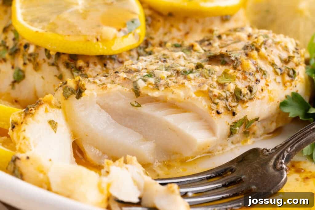Close up of baked cod showing flaky white interior topped with garlic herb butter and lemon slices.