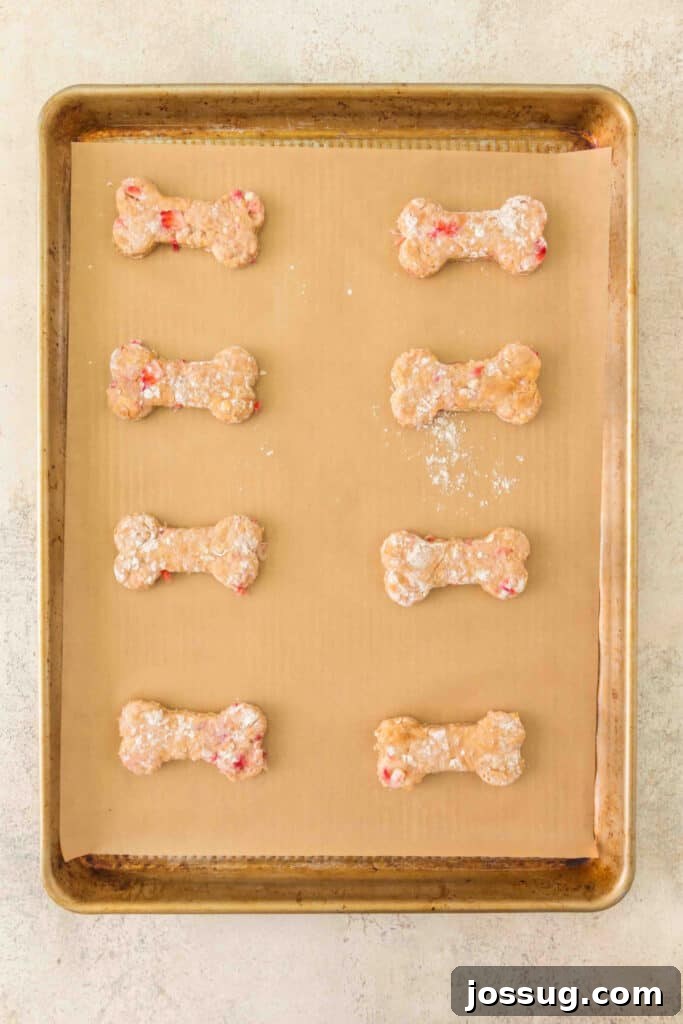 unbaked strawberry banana dog treats shaped like bones on a parchment-lined baking sheet