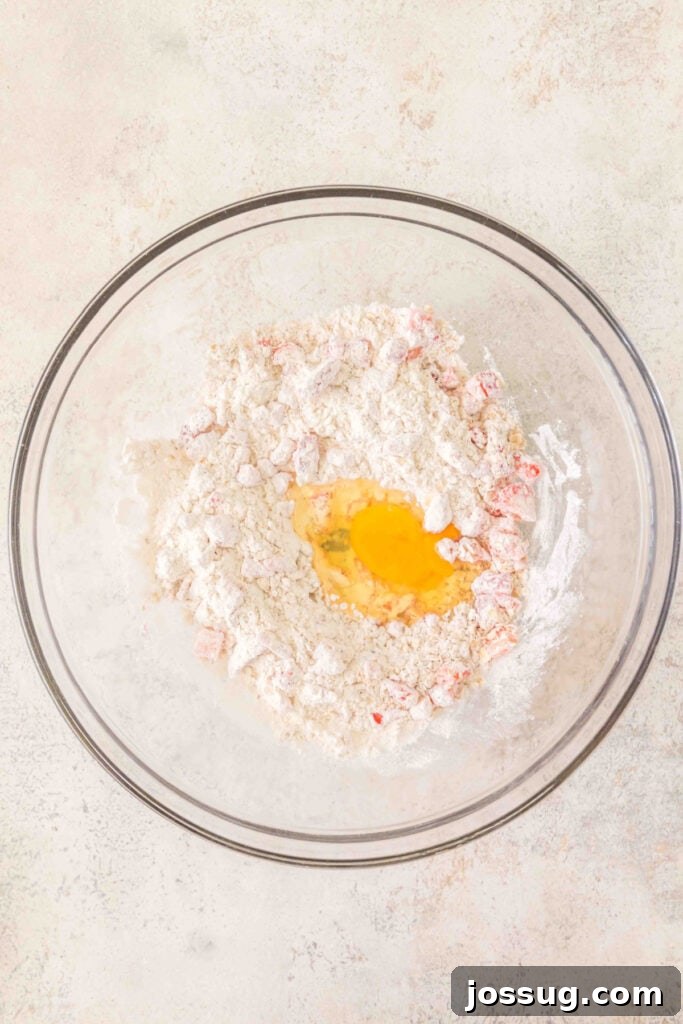 flour mixture with chopped strawberries in a bowl with a cracked egg added