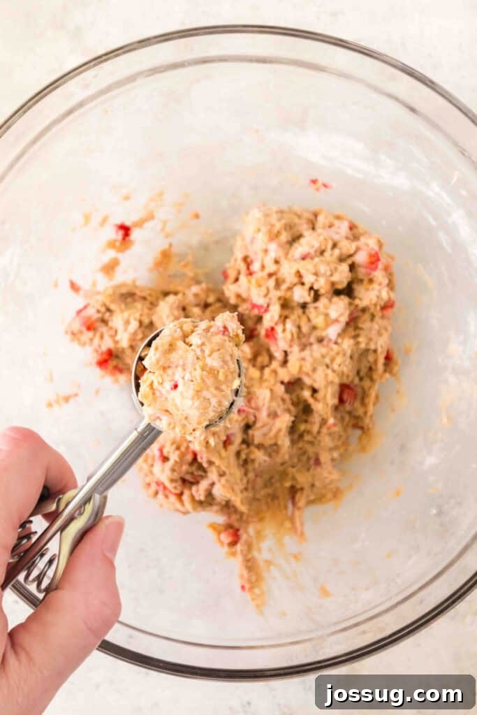scoop of strawberry banana dog treat dough held over a mixing bowl