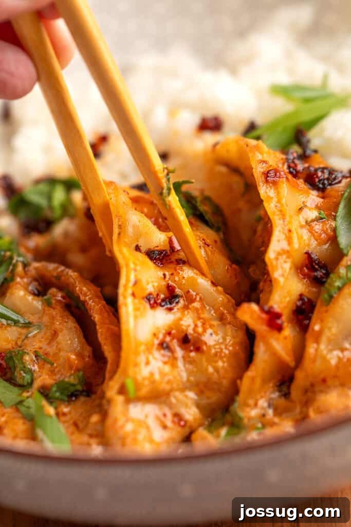 Chopsticks lifting a dumpling coated in coconut curry sauce with green onions and chili crunch