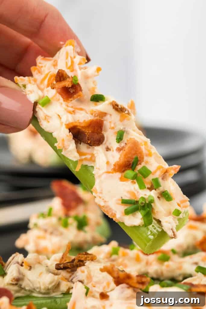 Close-up of a hand holding a celery stick filled with cheese, bacon, and chives