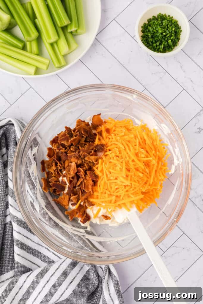 Shredded cheddar cheese and crumbled bacon added to cream cheese mixture in a glass bowl