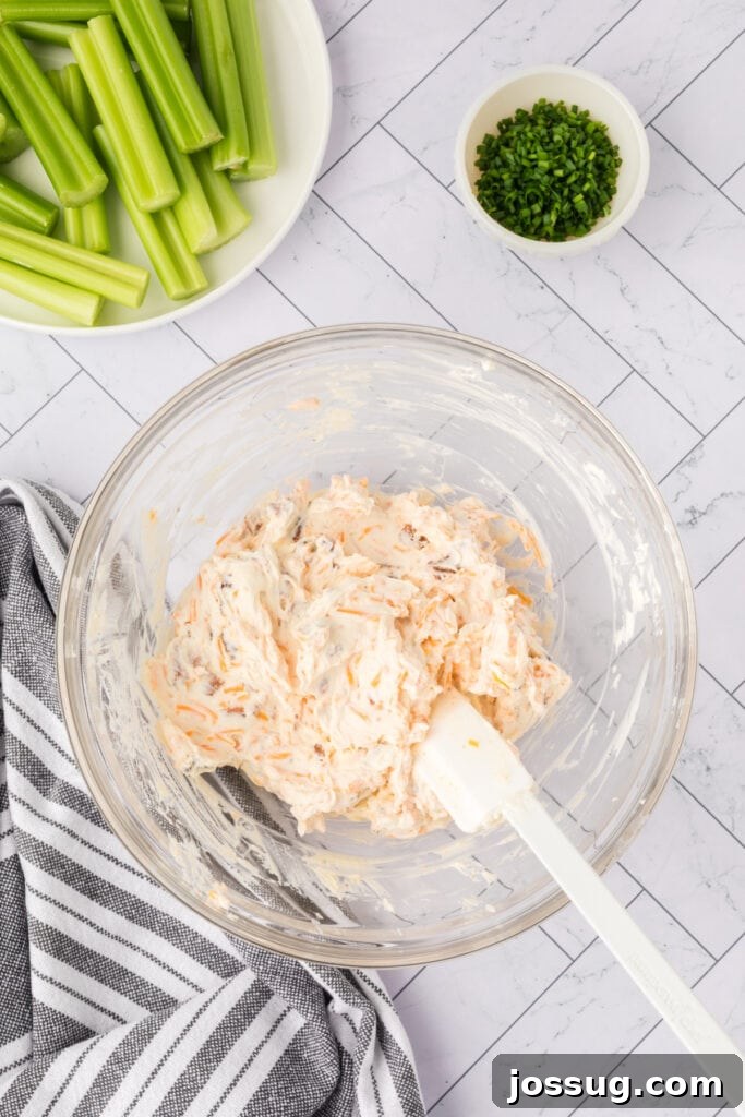 Cream cheese mixture fully combined with cheddar and bacon in a glass bowl