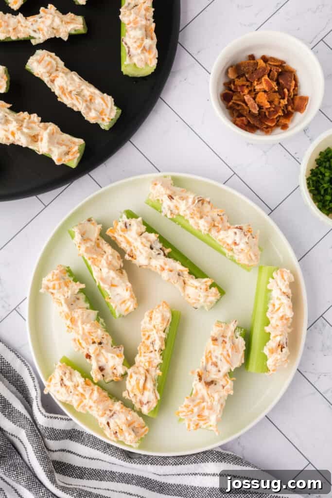 Celery sticks filled with cheese mixture on a plate with bowl of bacon and chives nearby