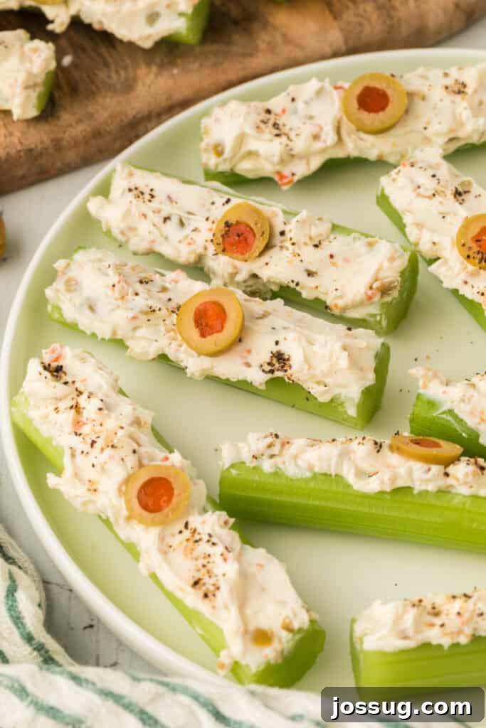 Close-up of stuffed celery sticks with cream cheese filling, olives, and black pepper on a plate