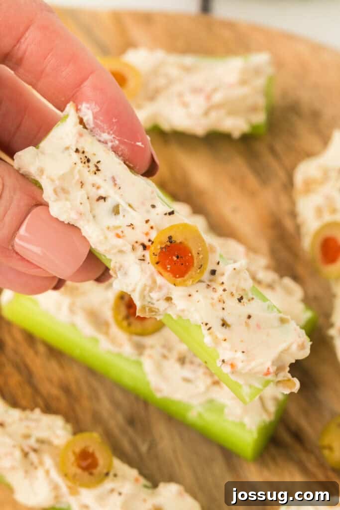 Hand holding a piece of stuffed celery topped with a sliced olive and black pepper