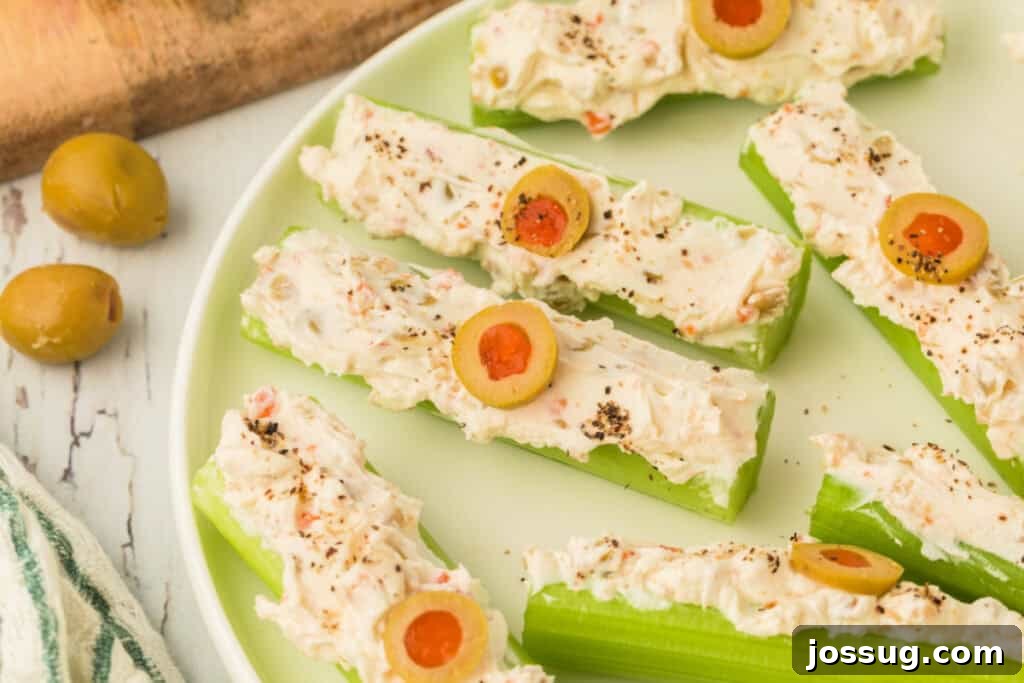 Close-up of stuffed celery on a plate topped with sliced olives and black pepper