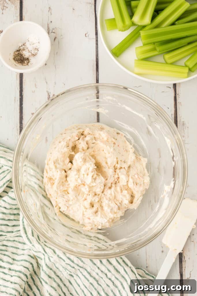 Cream cheese mixture fully combined in a glass bowl next to cut celery pieces