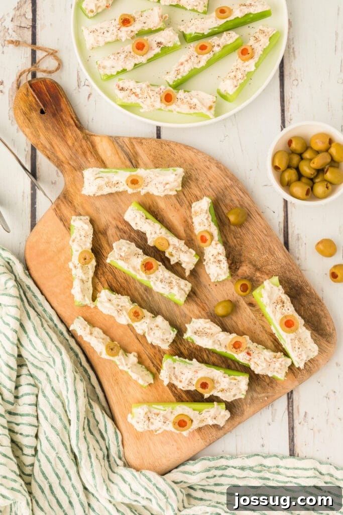 Stuffed celery arranged on a wooden board with sliced olives and seasoning nearby