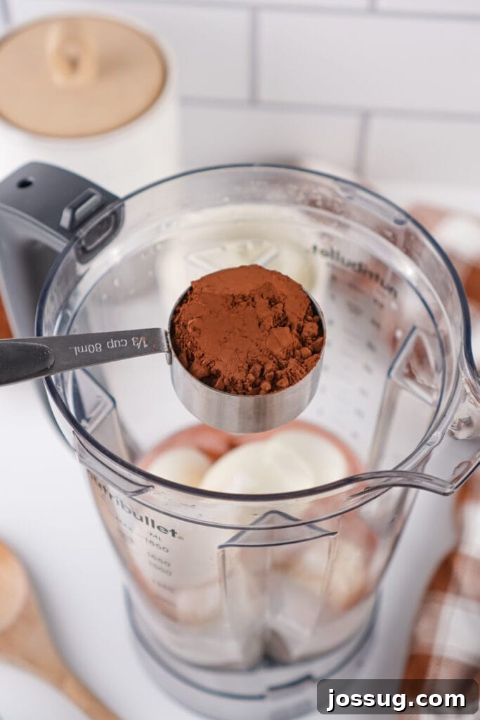 Chocolate Infused Custard Eggs 9 Measuring cup of cocoa powder held over blender with hard boiled eggs inside