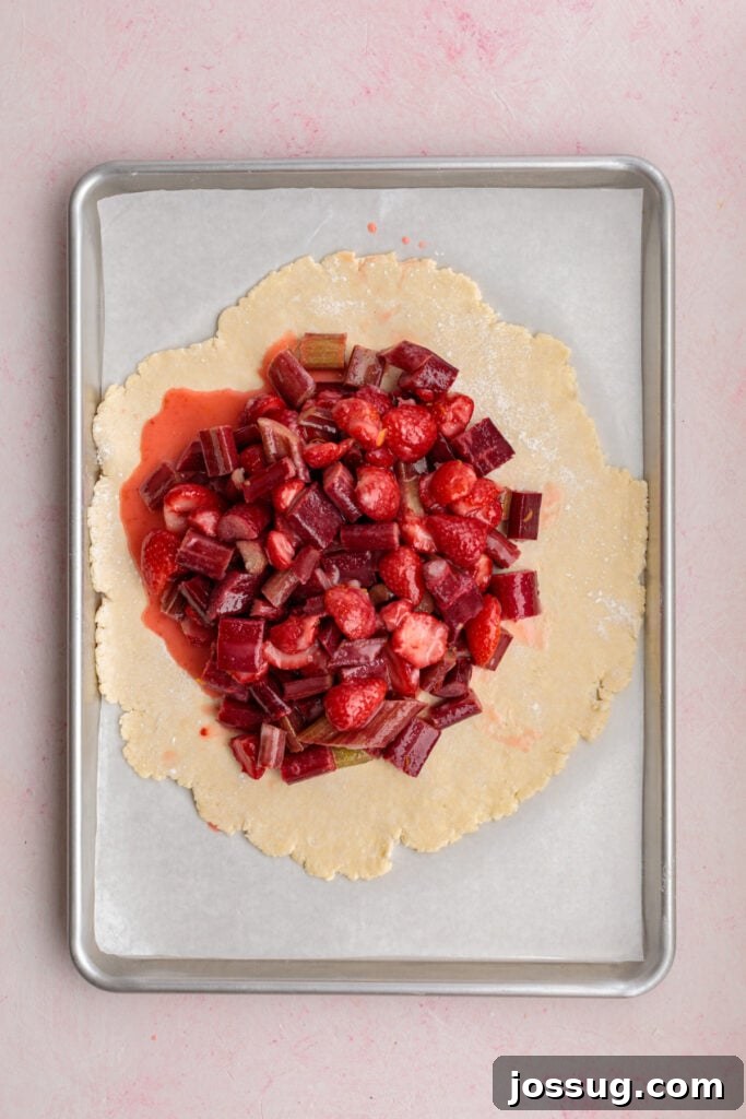 Simply Irresistible Strawberry Rhubarb Galette 14 The vibrant strawberry and rhubarb filling is piled artfully in the center of the rolled galette dough on a parchment-lined baking sheet, showcasing the generous border left for folding.