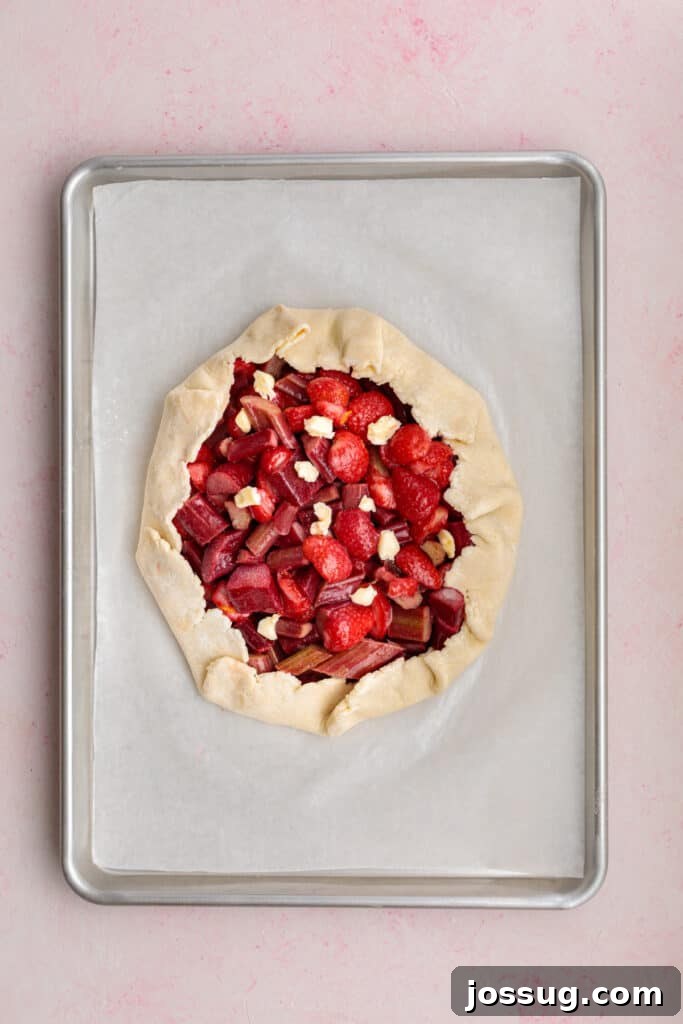 Simply Irresistible Strawberry Rhubarb Galette 16 An unbaked strawberry rhubarb galette, dotted with small pieces of butter scattered over the exposed fruit filling, ready to be brushed and baked to golden perfection.