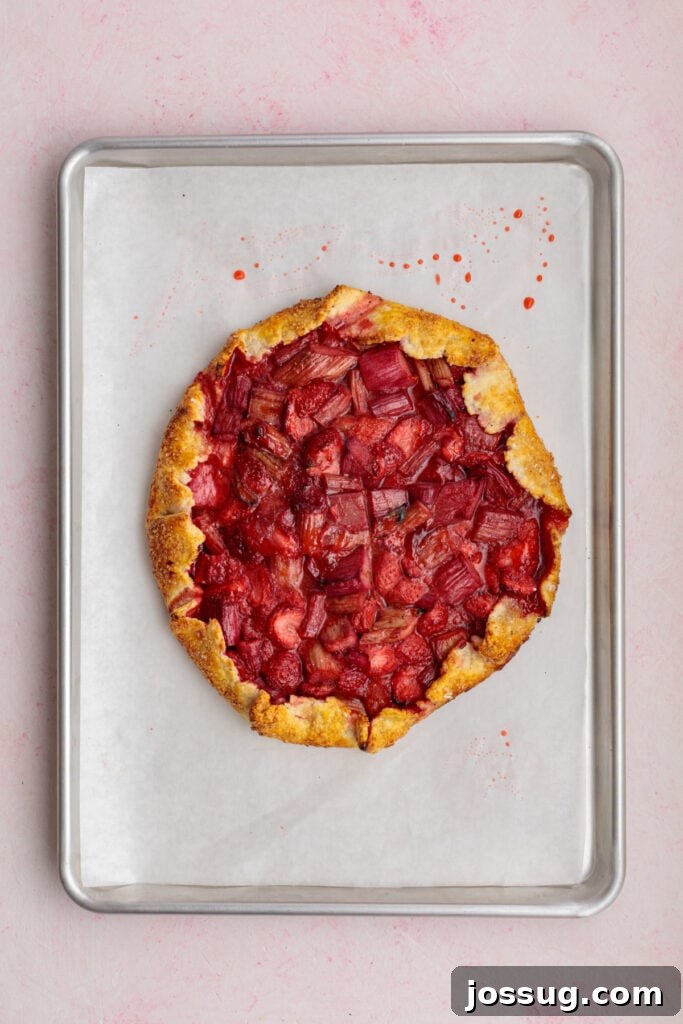 Simply Irresistible Strawberry Rhubarb Galette 19 A freshly baked strawberry rhubarb galette rests on a parchment-lined baking sheet, showcasing its perfectly golden, crisp crust and a delightfully bubbly fruit filling.