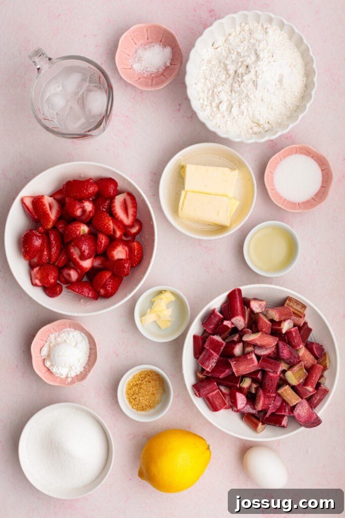 Simply Irresistible Strawberry Rhubarb Galette 3 An overhead view of all the pristine ingredients required for a homemade strawberry rhubarb galette, neatly arranged on a cheerful pink background. Visible elements include precisely sliced strawberries, freshly chopped rhubarb, all-purpose flour, cold butter cubes, granulated sugar, a bright lemon, an egg, and a glass of ice water, all ready for the baking process.