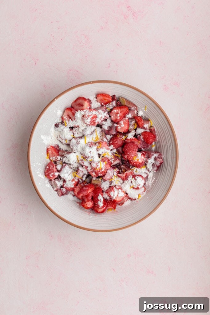 Simply Irresistible Strawberry Rhubarb Galette 10 Vibrant sliced strawberries and freshly chopped rhubarb are mixed with granulated sugar, cornstarch, and aromatic lemon zest in a bowl, illustrating the perfectly prepared fruit filling.