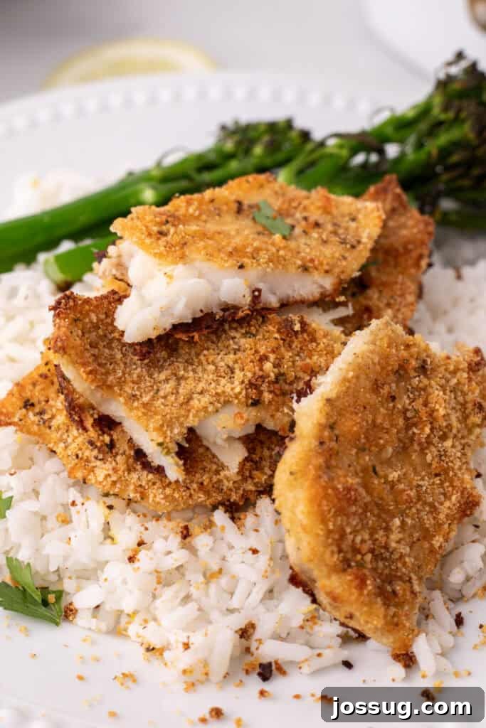 Close up of crispy baked garlic parmesan flounder pieces on white rice with crumbs visible, highlighting the texture.