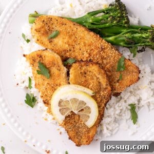 baked garlic parmesan flounder served on white rice with broccolini and a lemon slice on a white plate