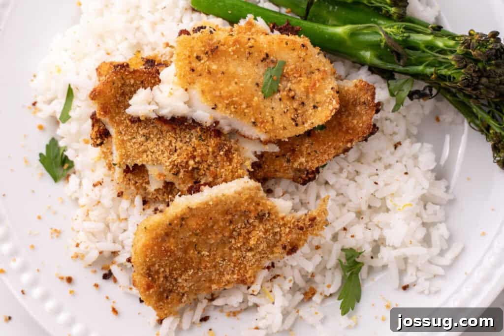 Close up of baked garlic parmesan flounder cut open on white rice with broccolini, showcasing its flaky texture and golden crust.